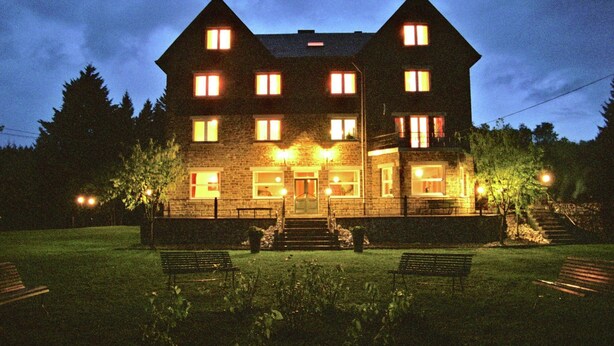 A large, multi-story stone building with a symmetrical facade, multiple windows, and a central entrance with steps. - Beautiful country house in the Ardennes with lots of privacy (Nisramont-La Roche)
