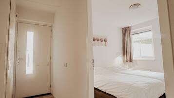 Un dormitorio con cama, ventana con cortinas, una lámpara de pared y una puerta.