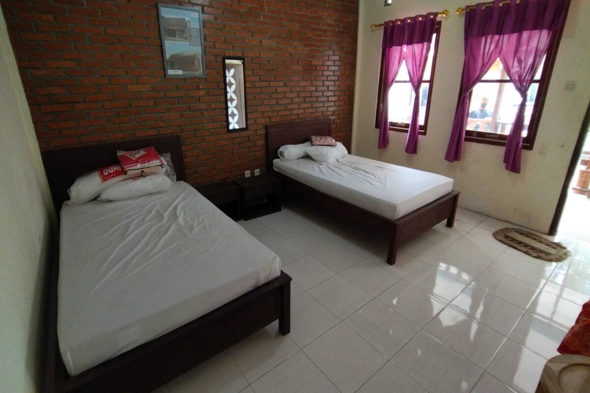 A room with two beds, a brick wall, and a window with purple curtains.