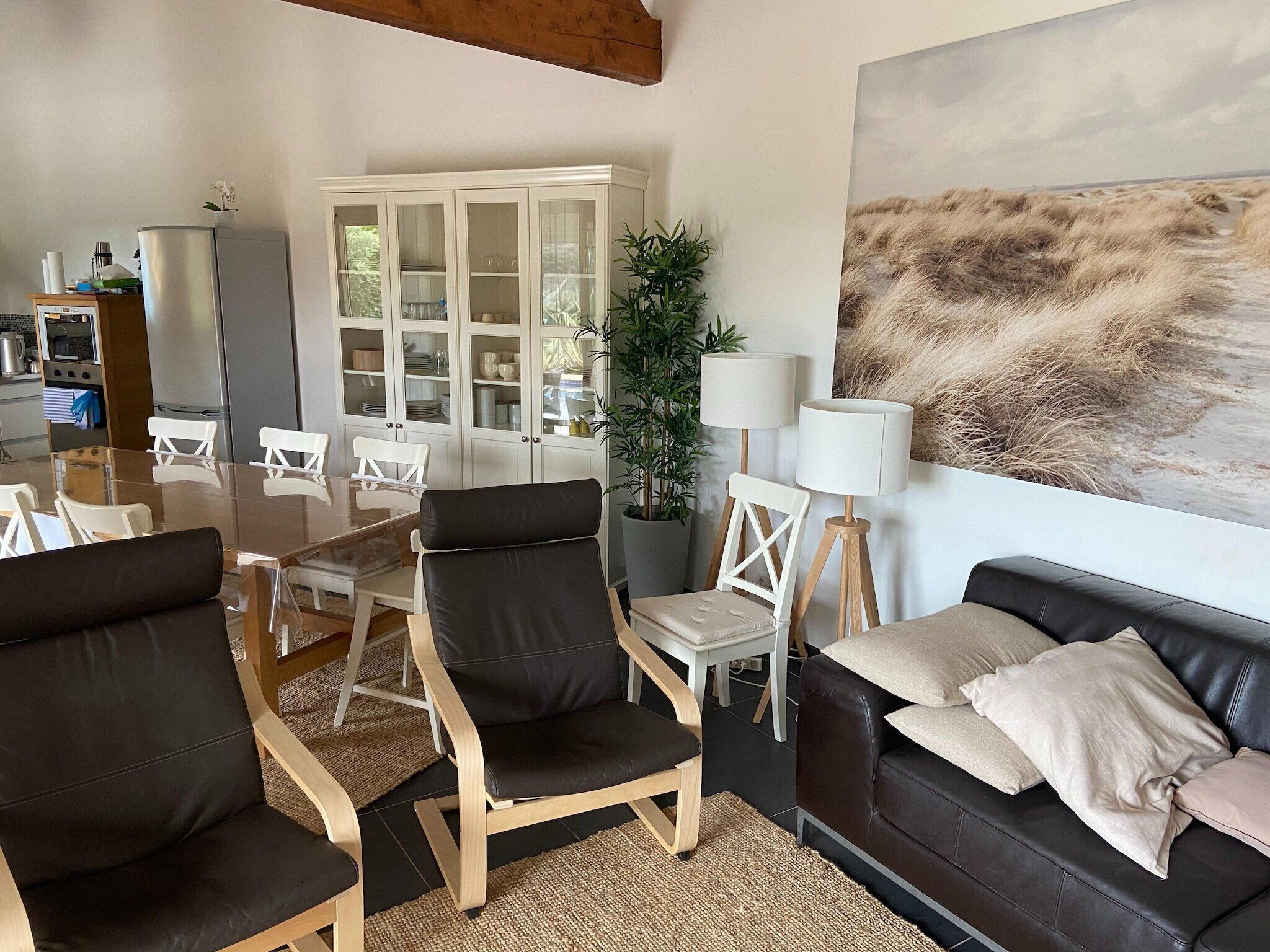 Ein modernes Wohnzimmer mit einem Glastisch, schwarzen Ledersesseln, Holzboden, einem beigen Sofa und einem großen abstrakten Gemälde.
