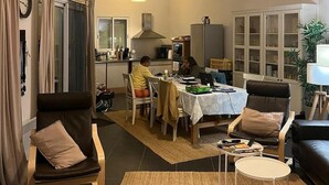 A spacious living area with a high ceiling and exposed wooden beams, a dining area with a table and chairs, and a kitchen in the background.