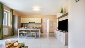 A modern kitchen with white cabinets, a dining table with chairs, a TV, and a potted plant. - Apartment 'Residence La Villa Principe' with Garden, Pool & Wi-Fi (Tignale Aer)