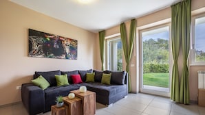 A modern living room with a sectional sofa, a coffee table, and a painting on the wall. - Apartment 'Residence La Villa Principe' with Garden, Pool & Wi-Fi (Tignale Aer)