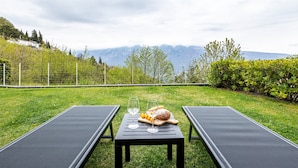 A table with a loaf of bread, two glasses of wine, and a baguette on a grassy lawn with two black lounge chairs. - Apartment 'Residence La Villa Principe' with Garden, Pool & Wi-Fi (Tignale Aer)
