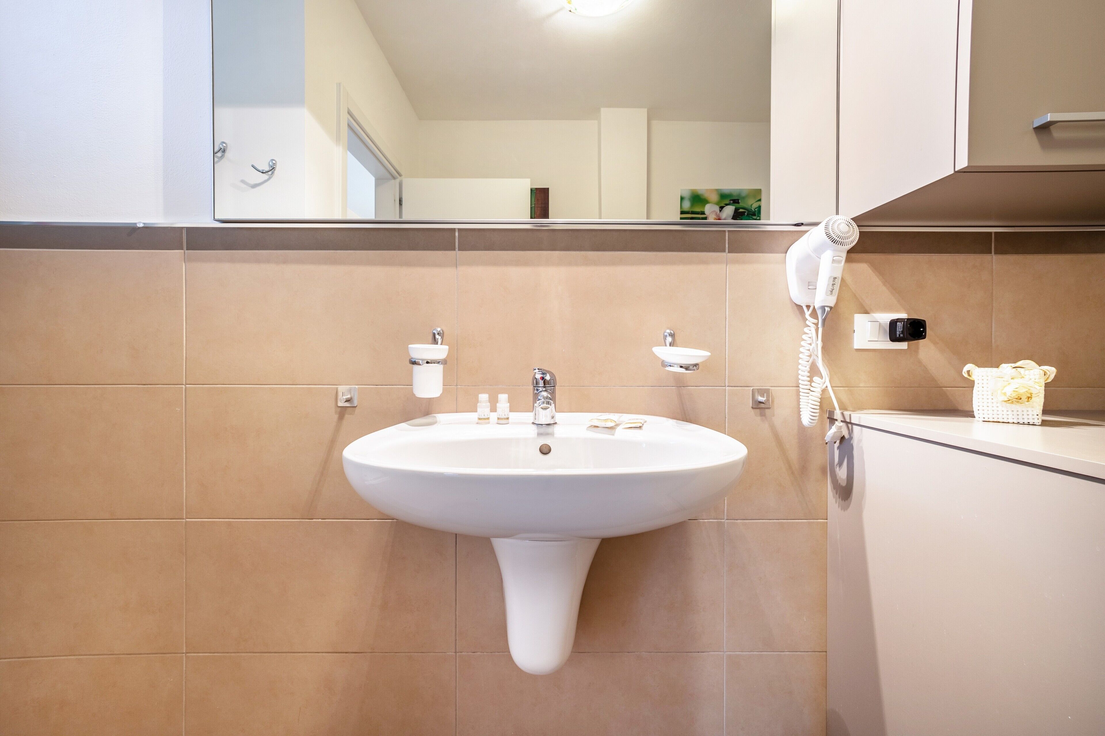 Ein Badezimmer mit einem weißen Waschbecken, einem Spiegel und einem Fön auf der Ablagefläche.