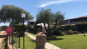Un sendero de piedra que conduce a un edificio con techo de tejas, rodeado de vegetación y una zona cercada.