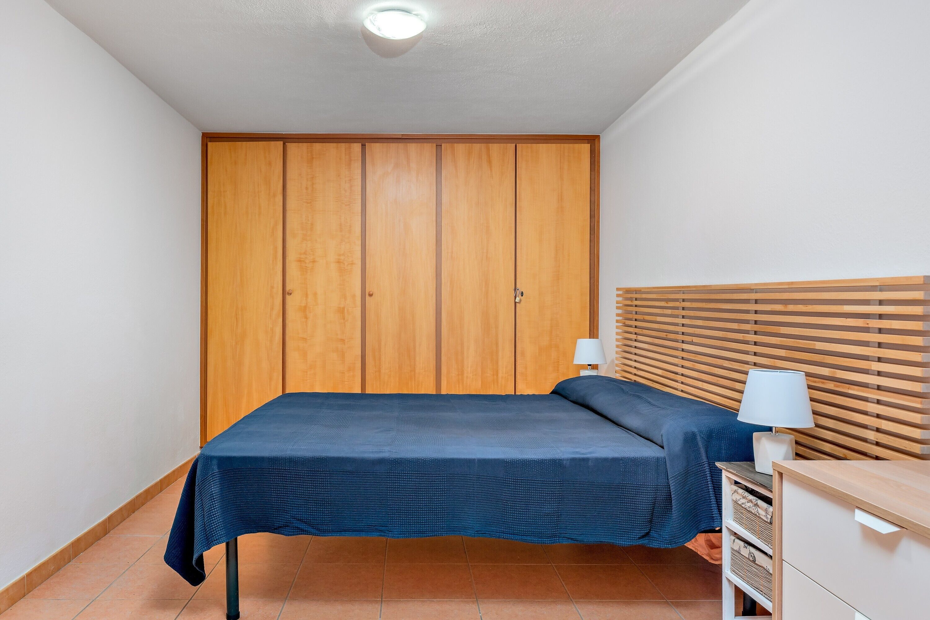Une chambre à coucher comprenant un lit, une armoire en bois, une table de chevet avec une lampe et une tête de lit.