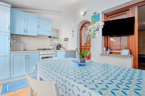 A kitchen with light blue cabinets, a dining table with a patterned tablecloth, and a TV mounted on the wall.