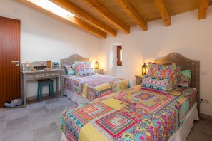 A bedroom with two beds, a desk, and a small stool.