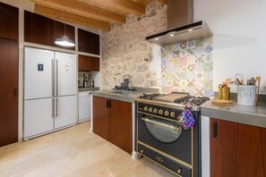 A kitchen with a stone wall, wooden cabinets, a gas stove, and a refrigerator.