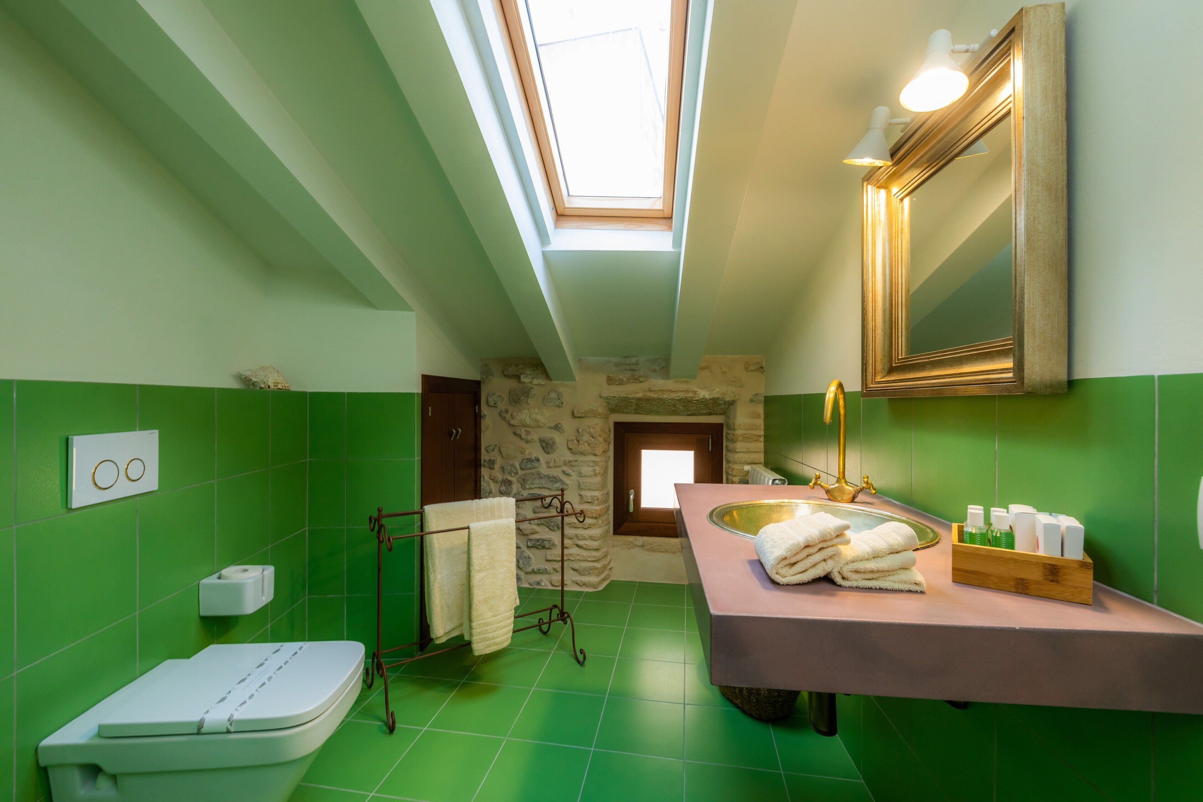 Un baño con tragaluz, pared de piedra, lavamanos con toallas y espejo.