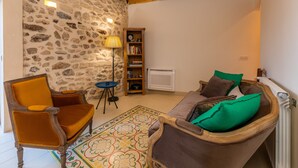 Ein Wohnzimmer mit Steinwand, Holzregal, Stehlampe, einer Couch mit Kissen und einem gemusterten Teppich.