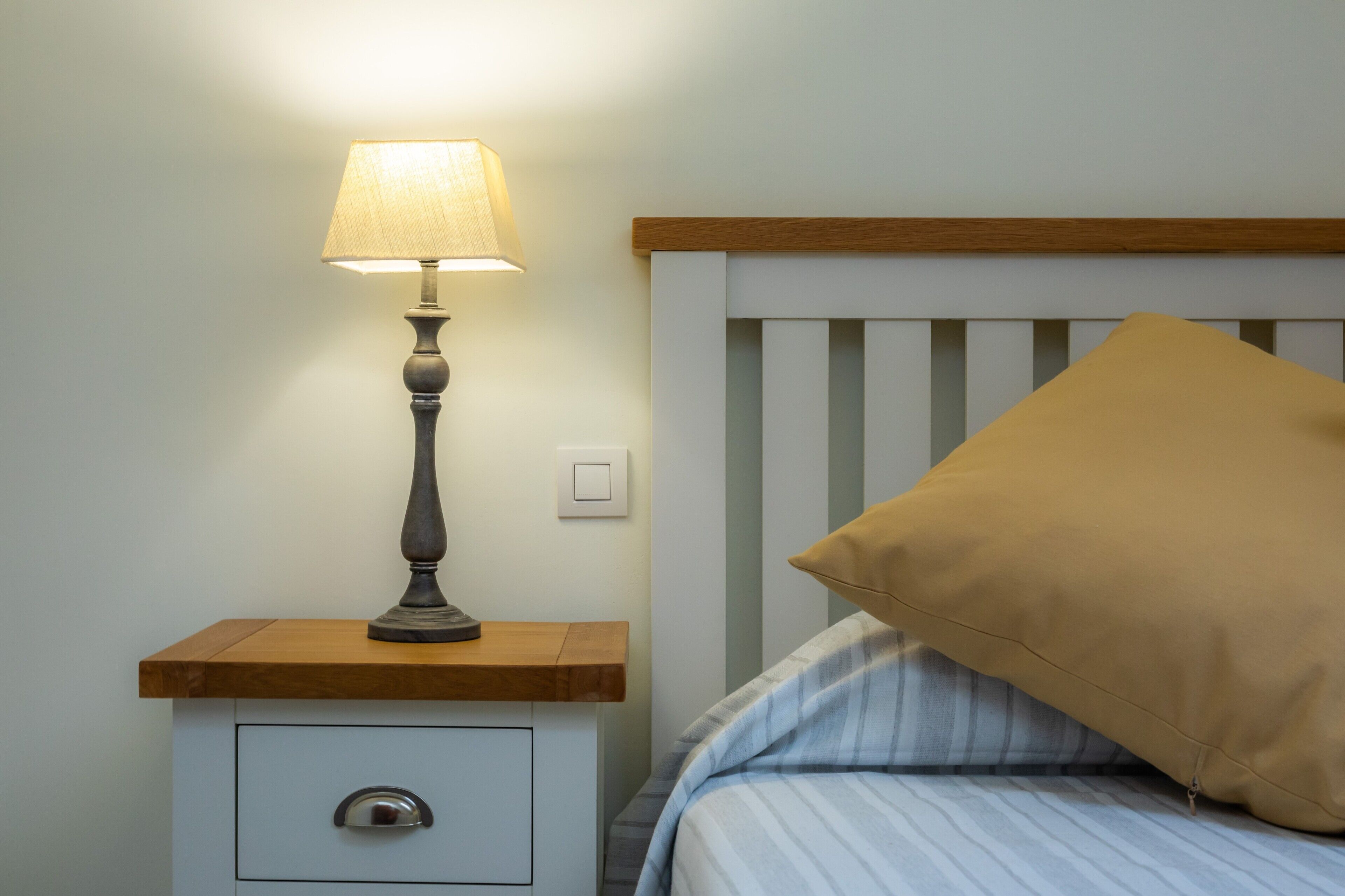 Un letto con lenzuola a righe blu e bianche, una testiera in legno e un cuscino beige.