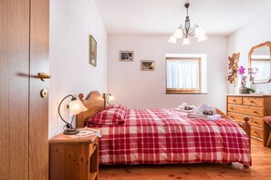 A bedroom with a wooden bed, a nightstand with a lamp, a dresser, and a window with curtains.