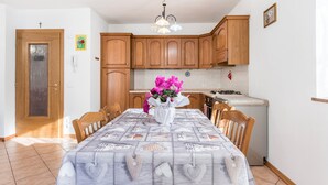 A dining area with a table set for four, wooden cabinets, a kitchen in the background, and a chandelier.