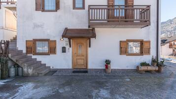 Un edificio de dos pisos con un balcón de madera, una puerta principal y una escalera que conduce a la entrada.