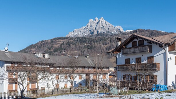 A mountain with a snow-covered peak, a white building with wooden balconies, and a clear blue sky.