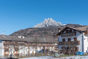 A mountain with a snow-covered peak, a white building with wooden balconies, and a clear blue sky.