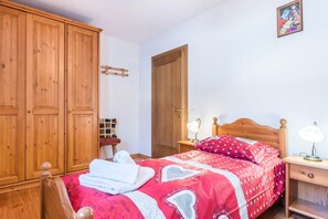 Une chambre avec une armoire en bois, un lit avec une literie rouge, une table de chevet avec des lampes et une porte.