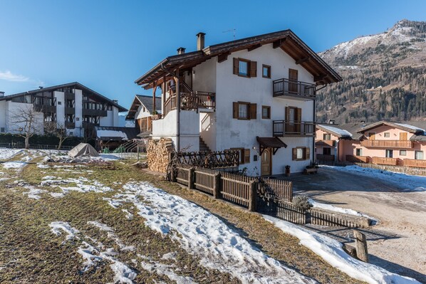 A two-story building with a balcony, a stone wall, and a mountain backdrop.