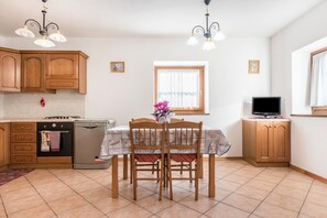 A kitchen with wooden cabinets, a dining table with chairs, a TV, and a window with curtains.