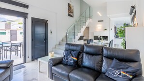 A modern living room with a leather sofa, a glass staircase, and a dining area.