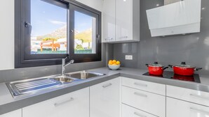 A modern kitchen with a stainless steel sink, white cabinets, a window with a view of buildings and mountains, and red pots on the countertop.