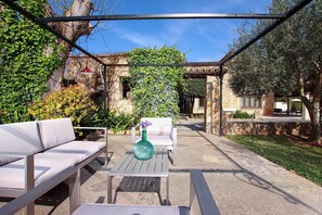 En udendørs terrasse med en hvid sofa, et bord med en vase og en pergola.