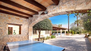 A ping pong table with a paddle, set against a stone wall with a wooden ceiling, surrounded by a paved patio area. - Country House 'Villa Papa' with Mountain View, Wi-Fi and Air Conditioning (Pollenca)
