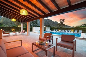 Un área de estar al aire libre con piscina, sillas de descanso y una mesa con una botella y vasos.