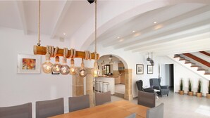A modern dining area with a wooden table and chairs, a unique rope light fixture, and a staircase leading to an upper level. - Country House 'Villa Papa' with Mountain View, Wi-Fi and Air Conditioning (Pollenca)