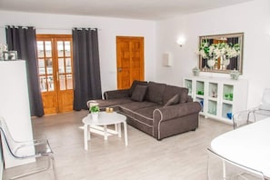 A living room with a grey sofa, a white coffee table, a white cabinet with glass doors, and a wooden door.