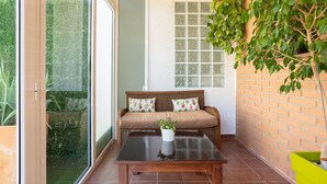 Una habitación con puerta de cristal corredera, un sofá marrón con cojines de cactus, una mesa de madera con una planta y una planta colgante.