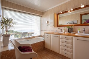 A bathroom with a bathtub, a sink, a mirror, and a potted plant.