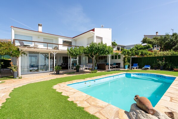 A modern house with a swimming pool, a covered patio, and a well-maintained lawn.