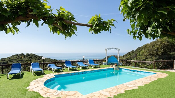 Una piscina con borde de piedra, rodeada de césped artificial y sillas de descanso azules.