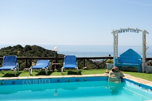 A pool with 'CAN DI LUCA' written on the edge, blue lounge chairs, and a view of the sea.