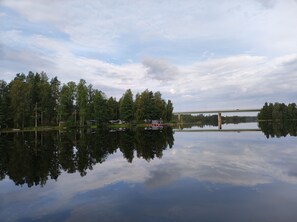 Un lac paisible avec un pont, entouré d’une forêt dense et sous un ciel dégagé.