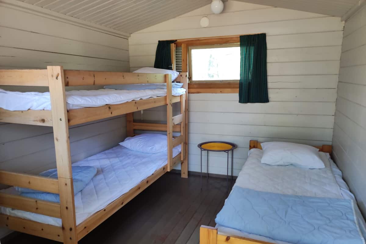 Una cabaña con tres literas, una mesita y una ventana con cortinas.