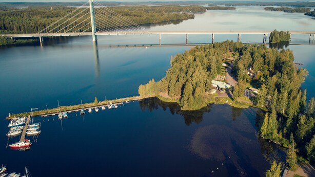 Luchtbeeld van een brug over een kalm meer, met een steiger en boten.