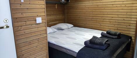 A small, wooden-paneled room with a single bed, a small shelf, and a door with a lock.