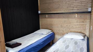 Een kleine, compacte kamer met twee eenpersoonsbedden, elk voorzien van een kussen en een opgevouwen handdoek. De kamer heeft een houten wand en een zwart paneel aan de zijkant.