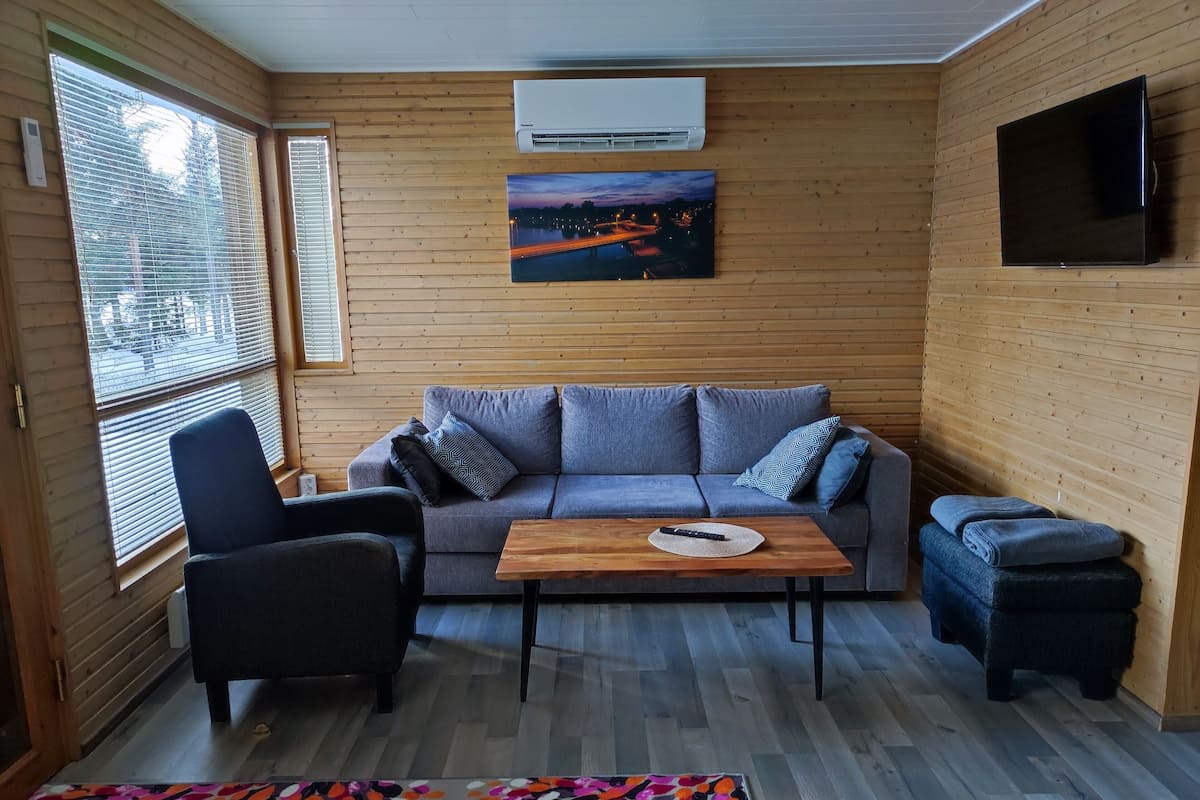 Una habitación acogedora con un sofá gris, una mesa de centro de madera, un sillón negro y una alfombra colorida.