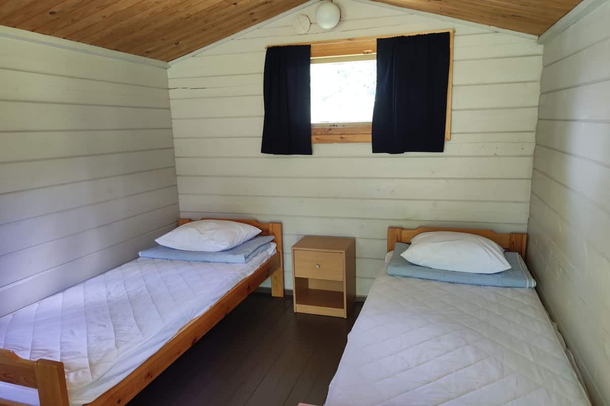 Una cabaña con dos camas literas de madera, una mesita de noche pequeña de madera y una ventana con cortinas.