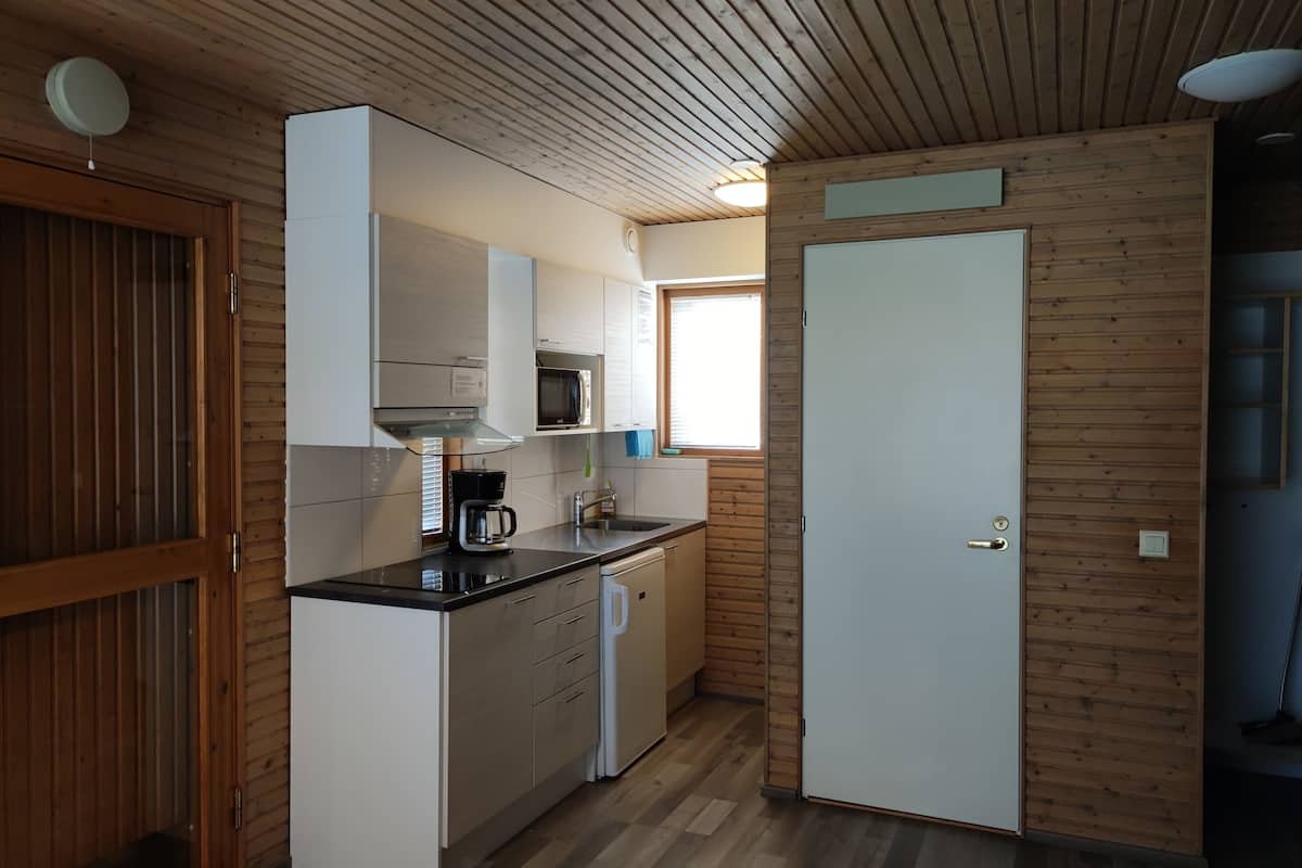 Cocina compacta con paneles de madera, microondas, cafetera y puerta que da a otra habitación.