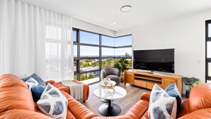 A modern living room with orange sofas, a round coffee table, and a large flat-screen TV.
