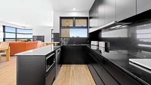 A modern kitchen with black cabinetry, a wooden floor, and a large window offering a view.