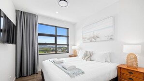 A hotel room with a large bed, a window with a view, a flat-screen TV, and a bedside table with a lamp.