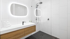 A modern bathroom with a white vanity, a wooden cabinet, a large mirror, and a shower with a handheld showerhead.