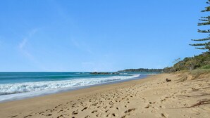 A wide sandy beach with visible footprints, a calm sea, and a clear sky. - Casa Bella - Luxury 3 Bedroom Rural Retreat (Coffs Harbour)